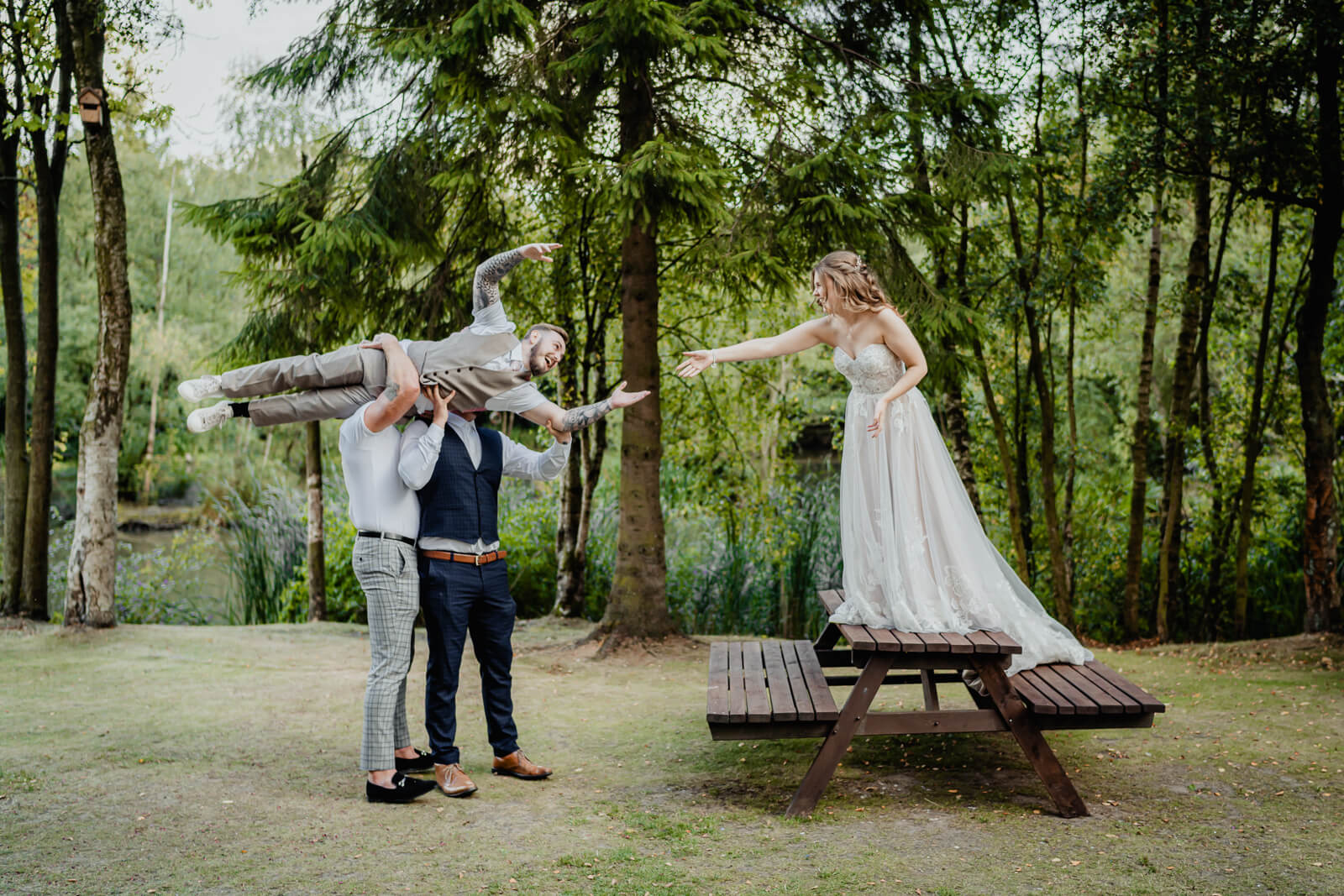 Fun wedding photo of groom lifted by groomsmen reaching toward bride at Chevin Country Park