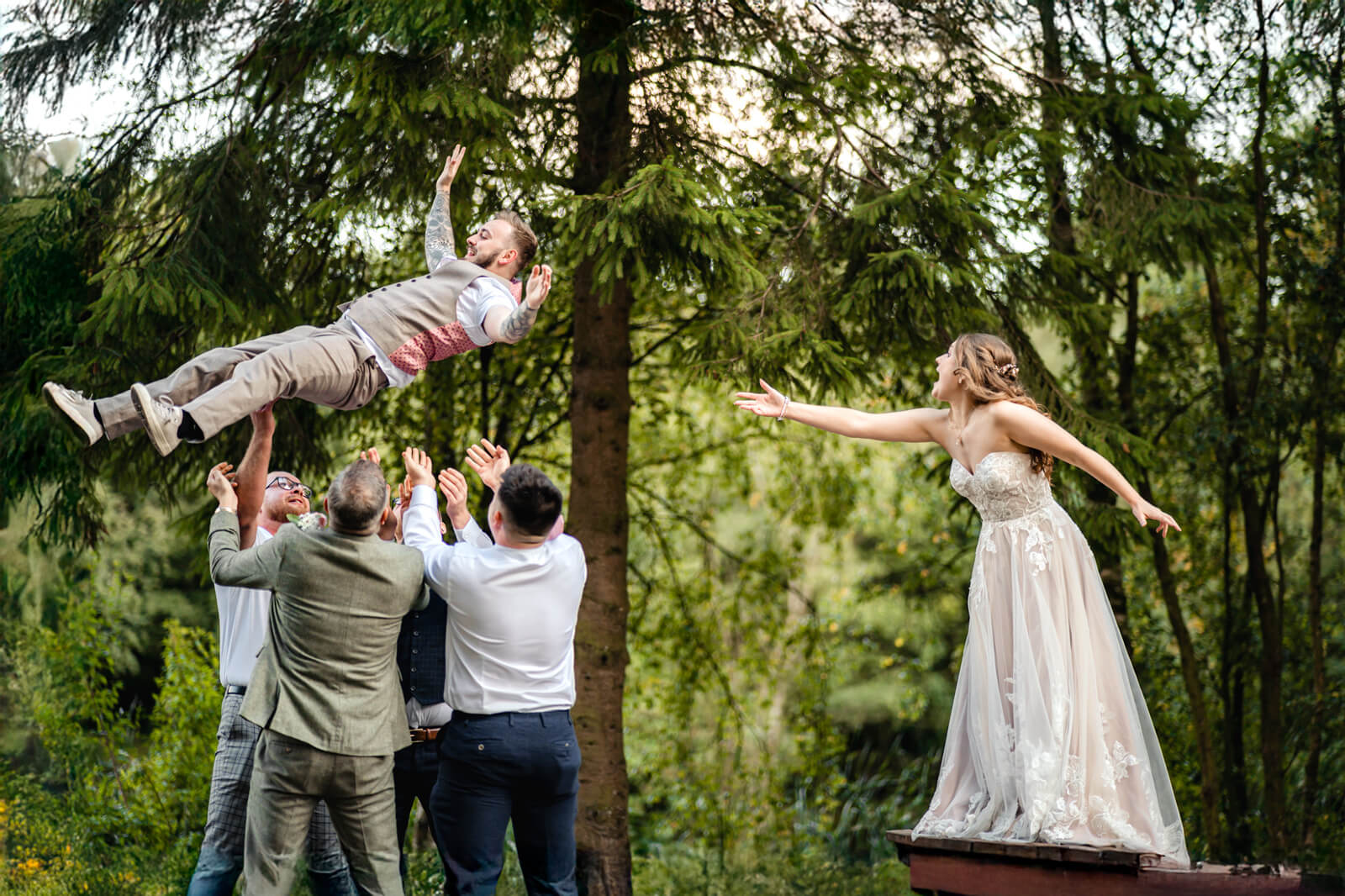 Groom tossed into the air by groomsmen while the bride reaches toward him