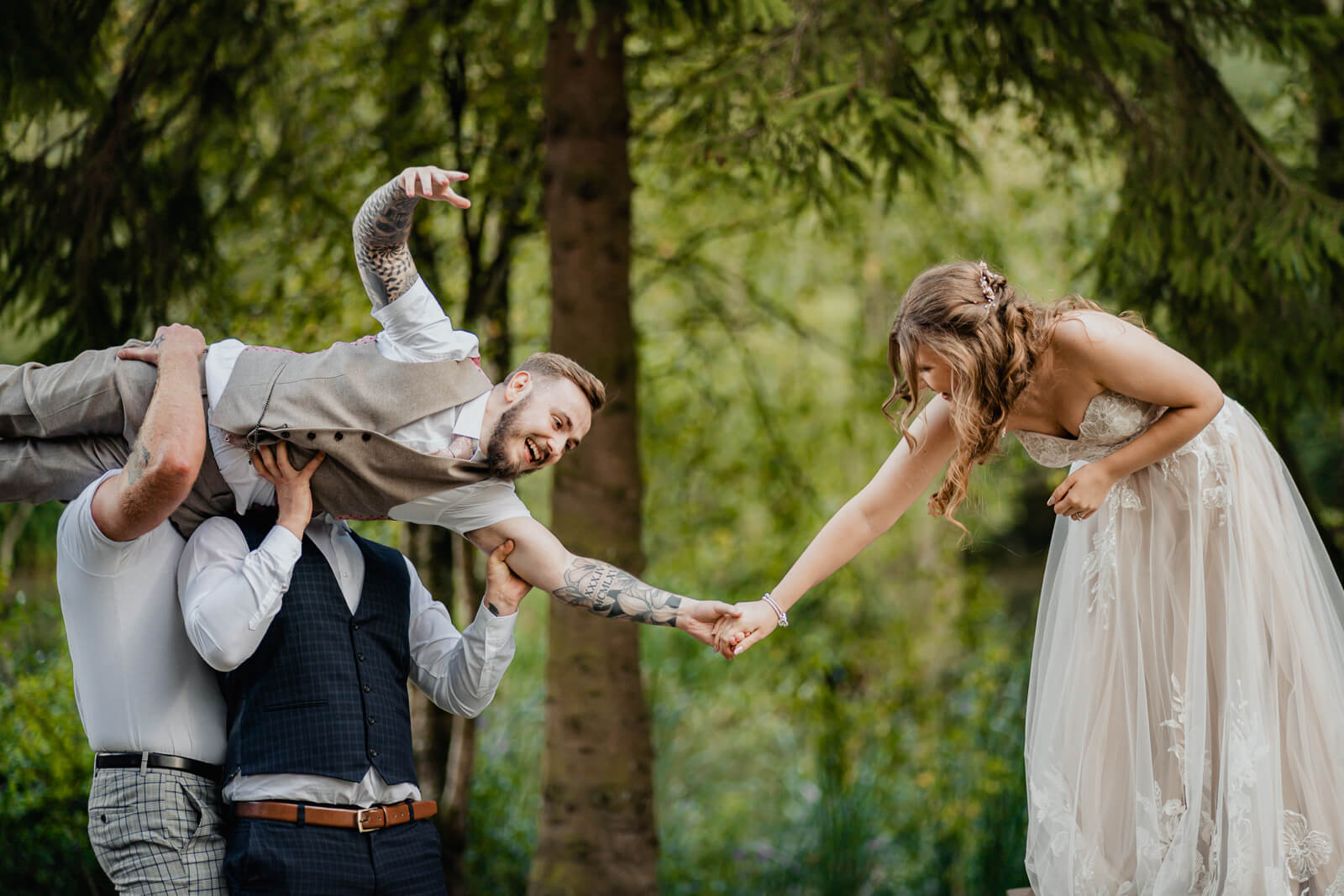 Bride and groom holding hands while groomsmen lift groom at Chevin Country Park