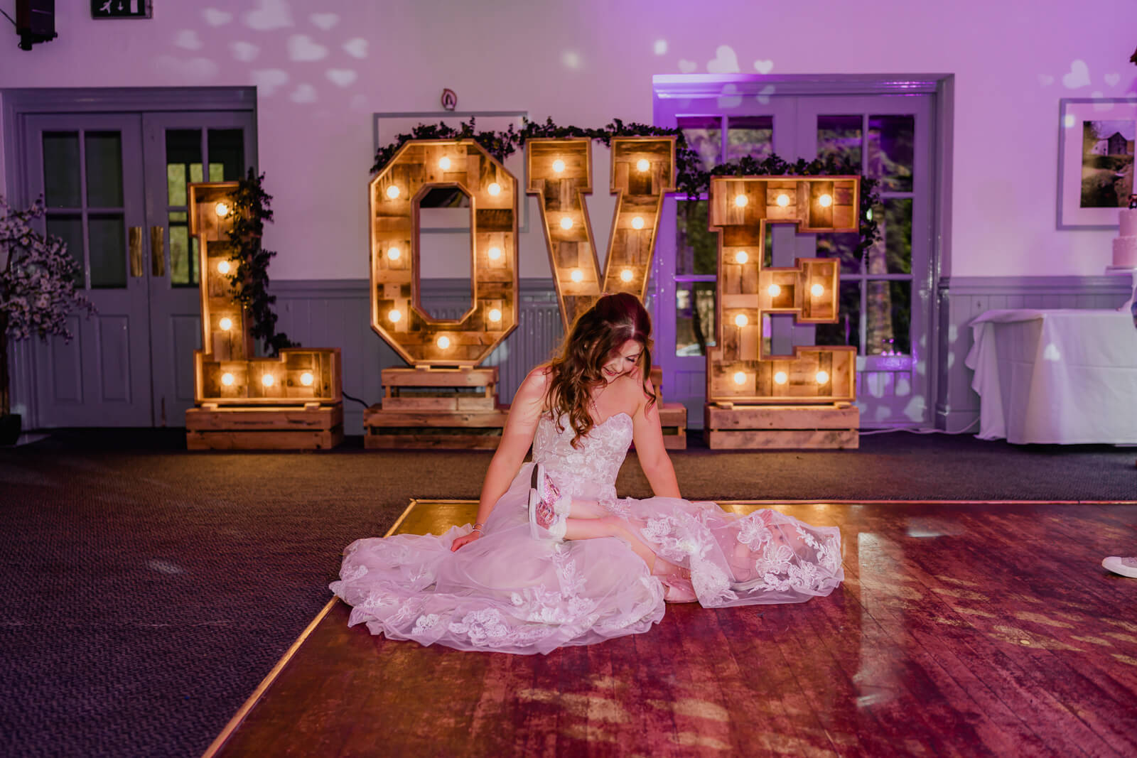 Bride sitting on dance floor in front of LOVE letters at Chevin Country Park wedding reception