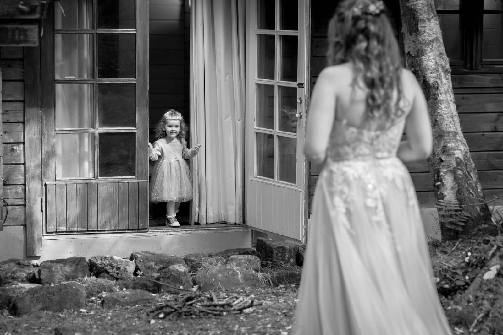 Flower girl standing in a doorway looking at the bride outside