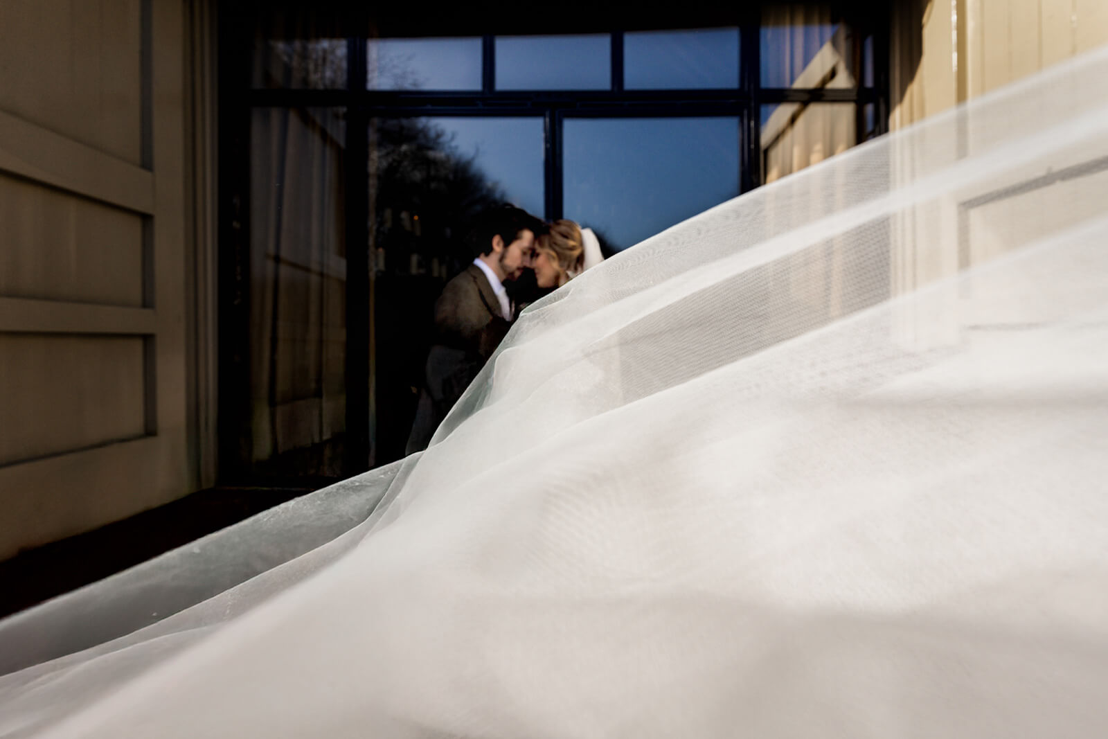Bride and groom embracing with flowing veil in foreground at a Yorkshire wedding venue - fine art editorial wedding photography