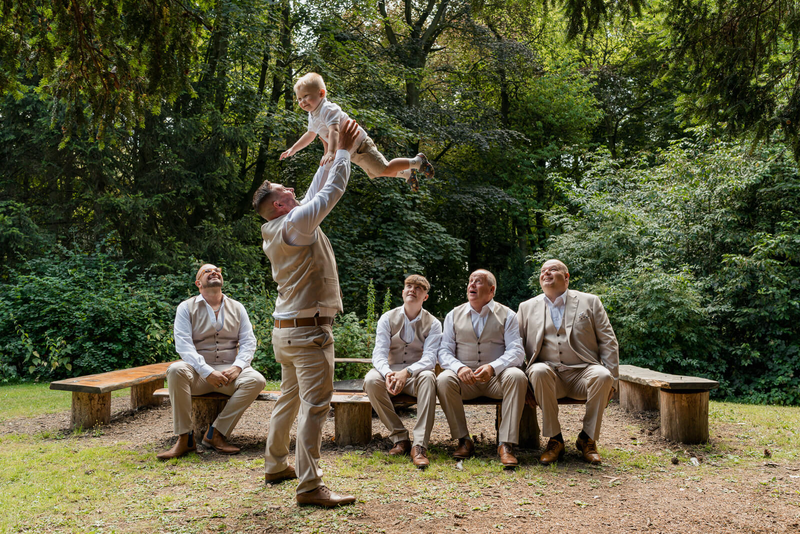 Groom lifts a young child into the air before a Hazlewood Castle woodland wedding ceremony.