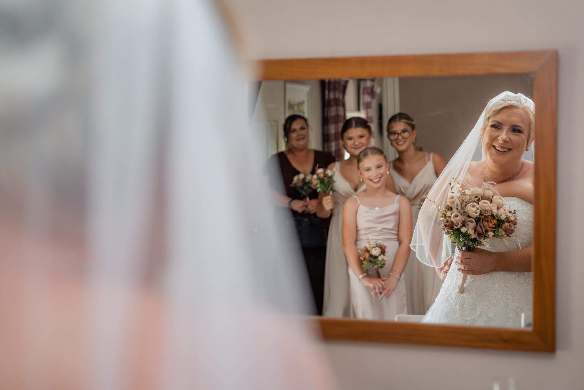 Bride smiling at her reflection with bridesmaids behind her.