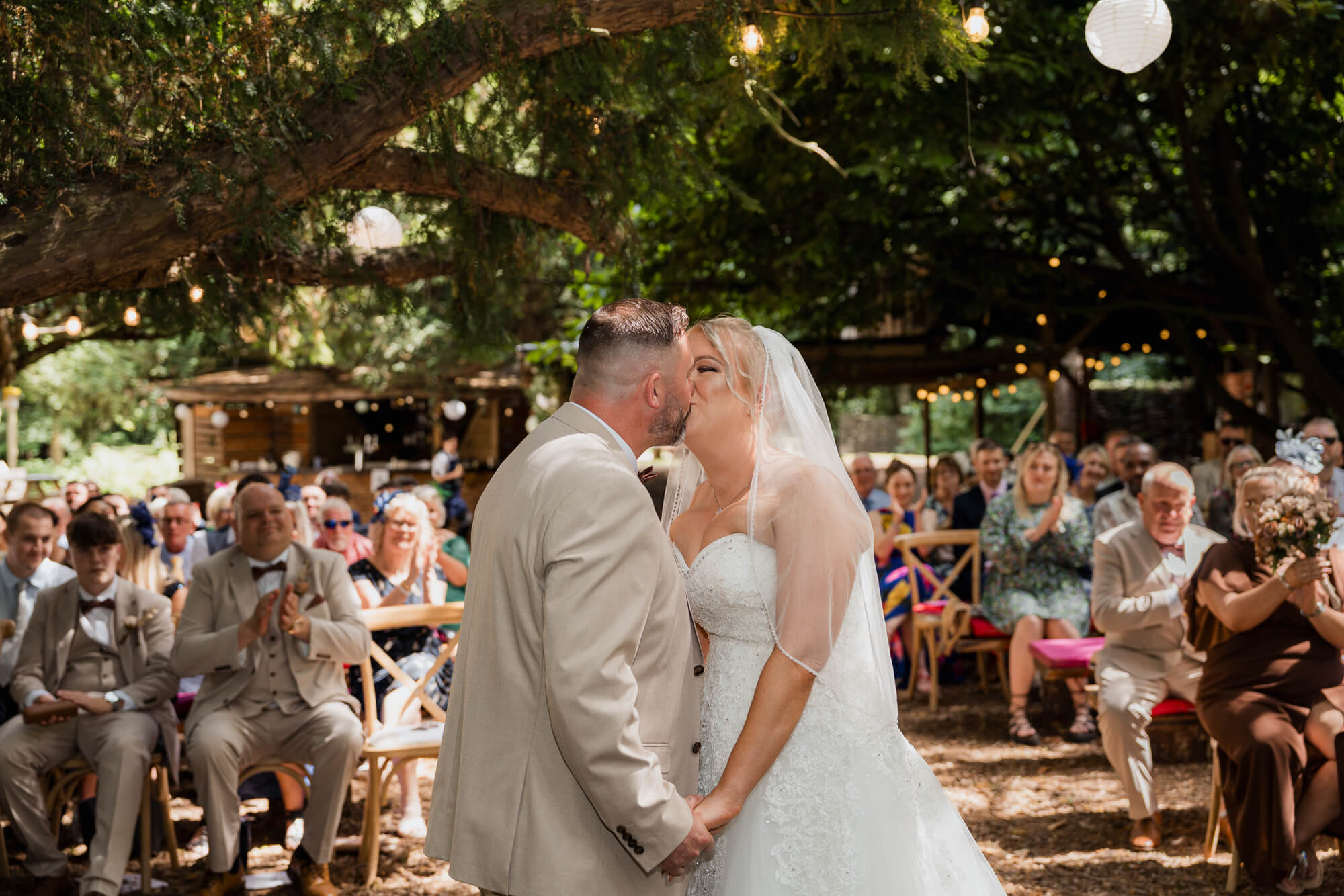 Bride and groom sharing their first kiss during the woodland wedding ceremony.