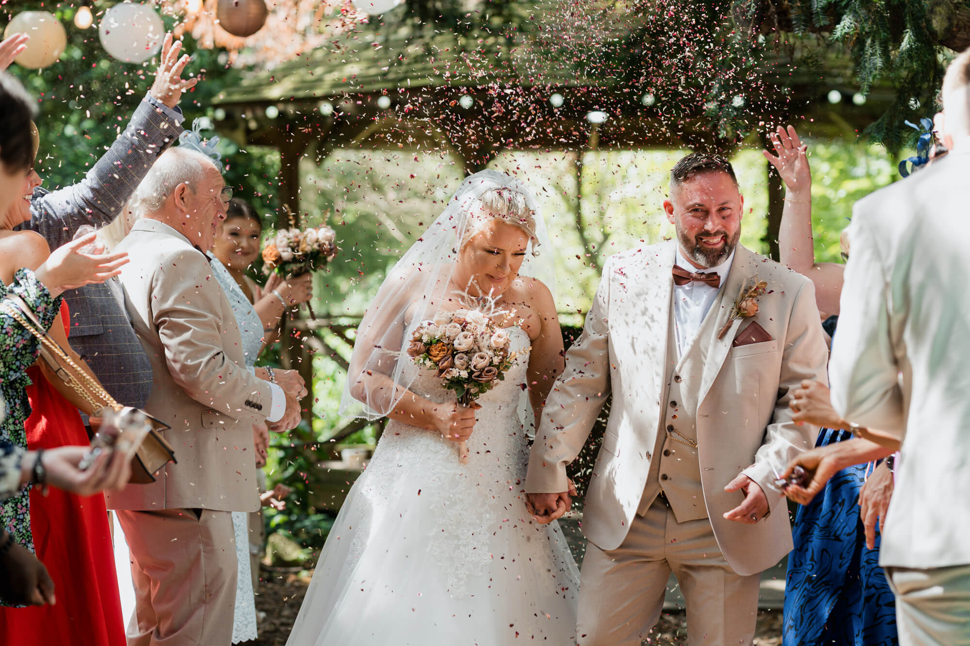 Bride and groom walking through confetti after their woodland wedding ceremony.