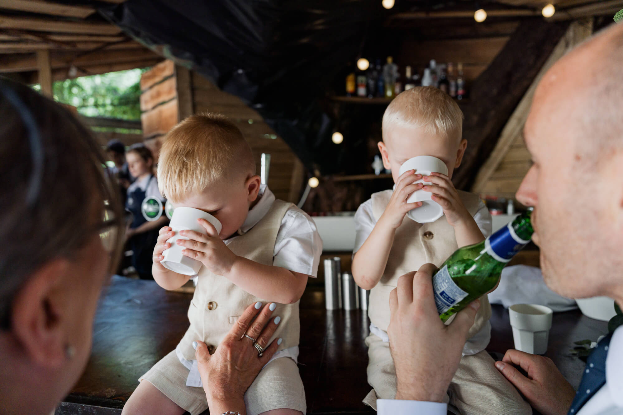 Two young page boys drinking from paper cups during the wedding reception.