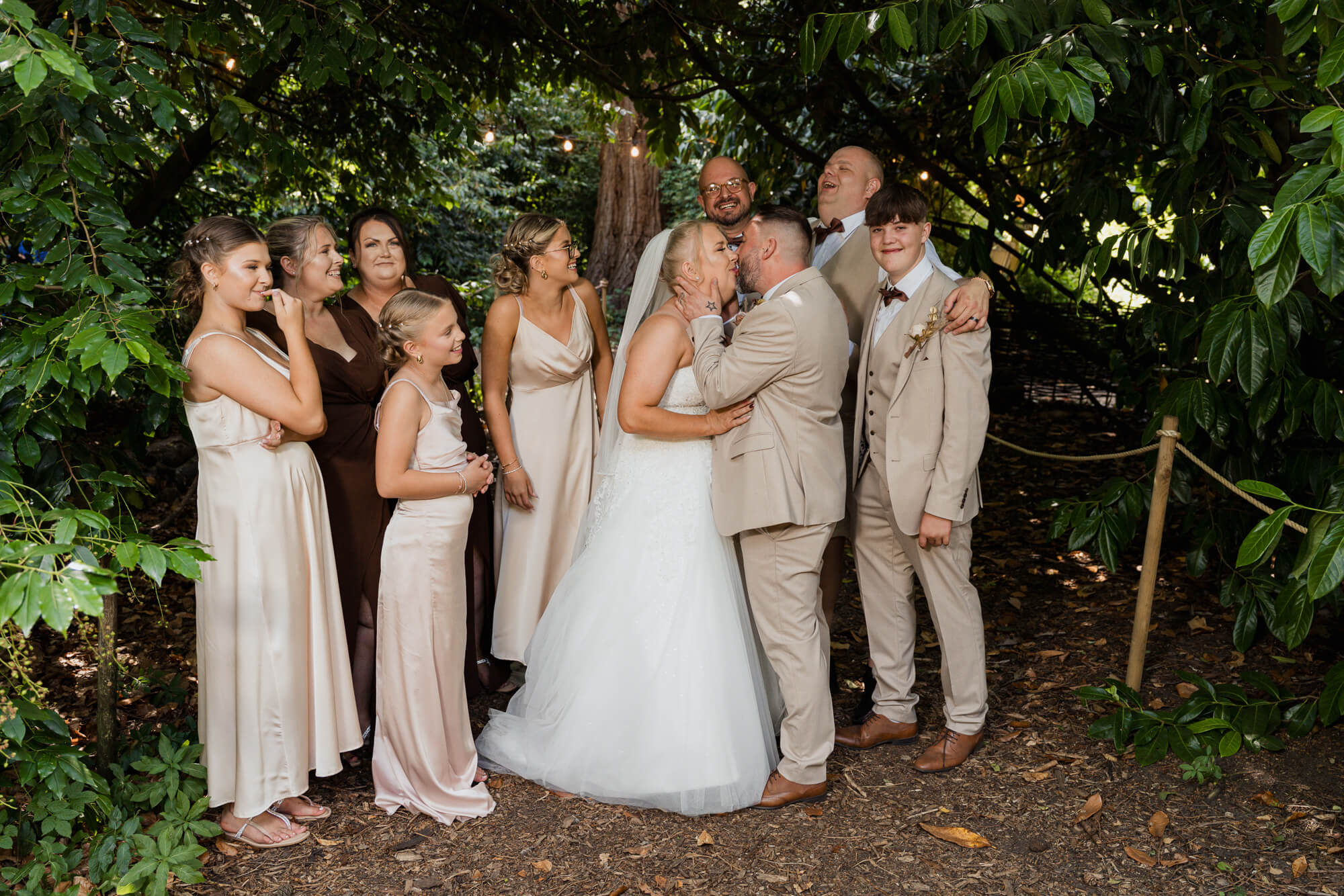 Bride and groom kissing with family during woodland wedding portraits at Hazlewood Castle.