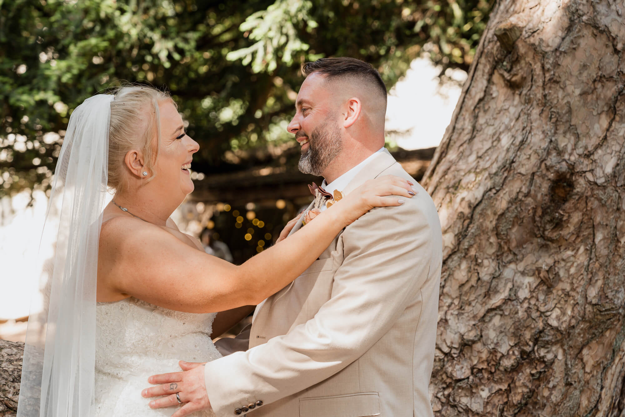Bride and groom laughing together beneath a woodland tree at Hazlewood Castle.