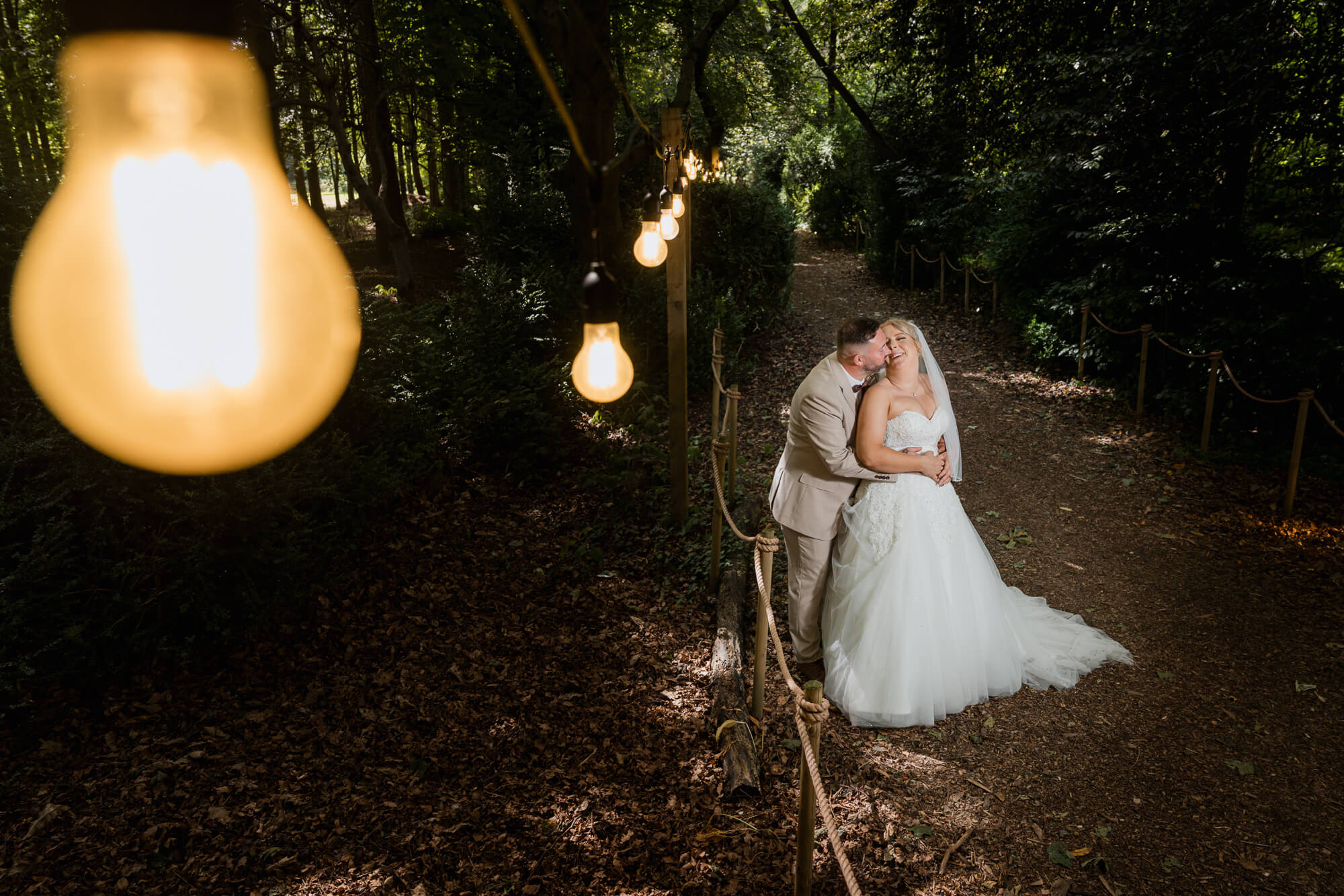Bride and groom embracing beneath the woodland lights at Hazlewood Castle.