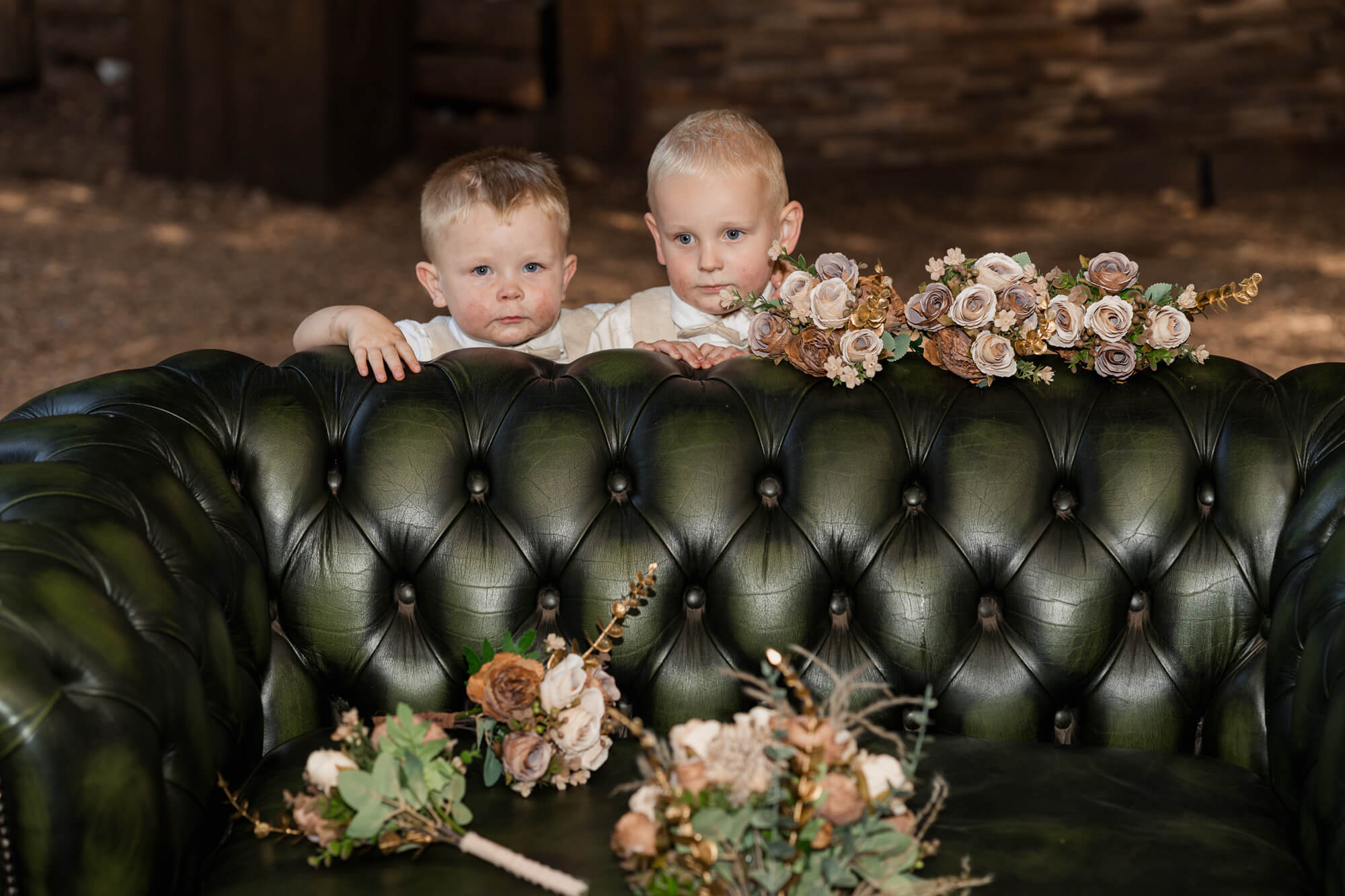 Two young page boys standing behind a green leather sofa.