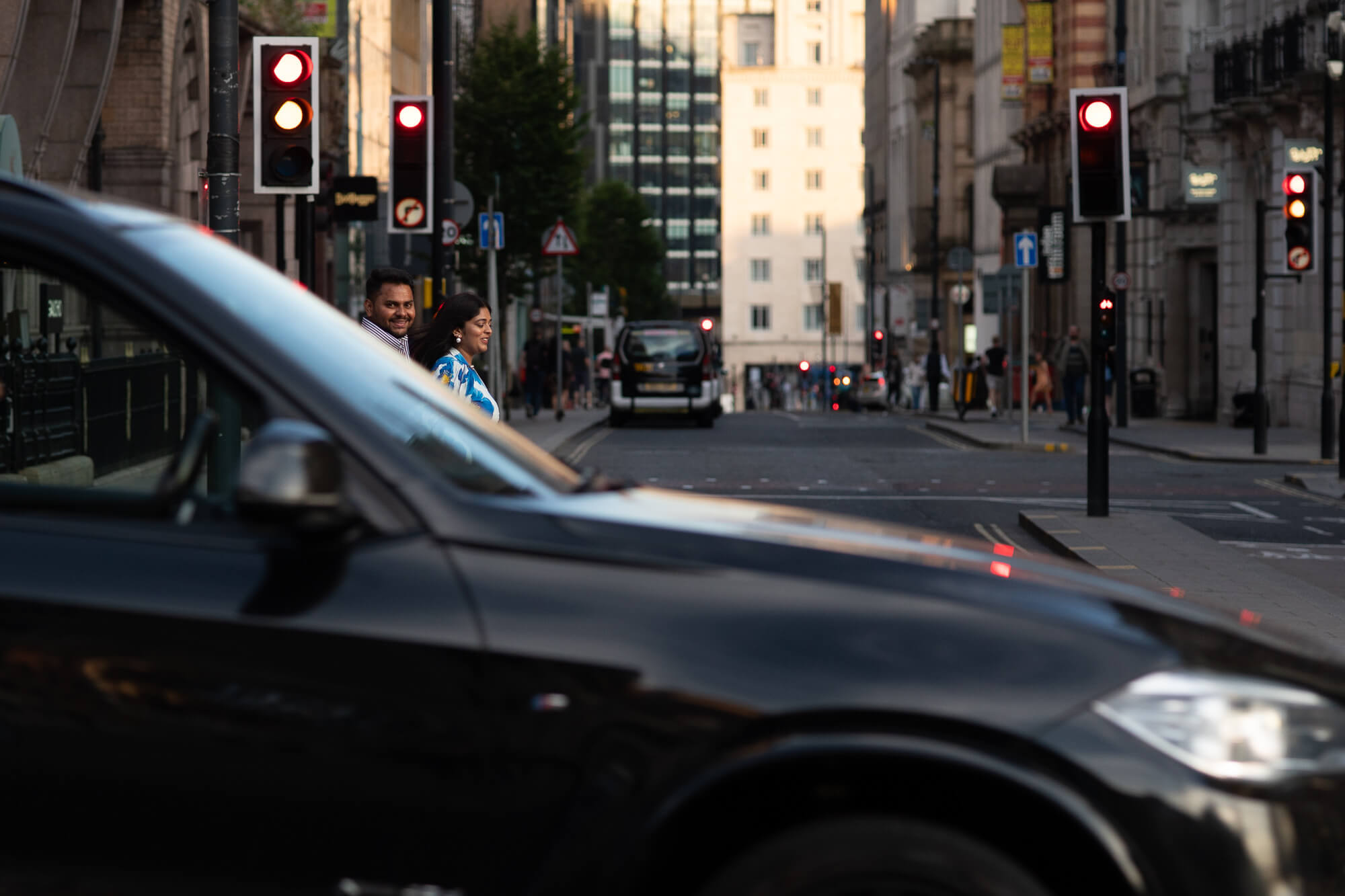 Creative engagement photo with a passing car framing a couple crossing the street in Leeds.