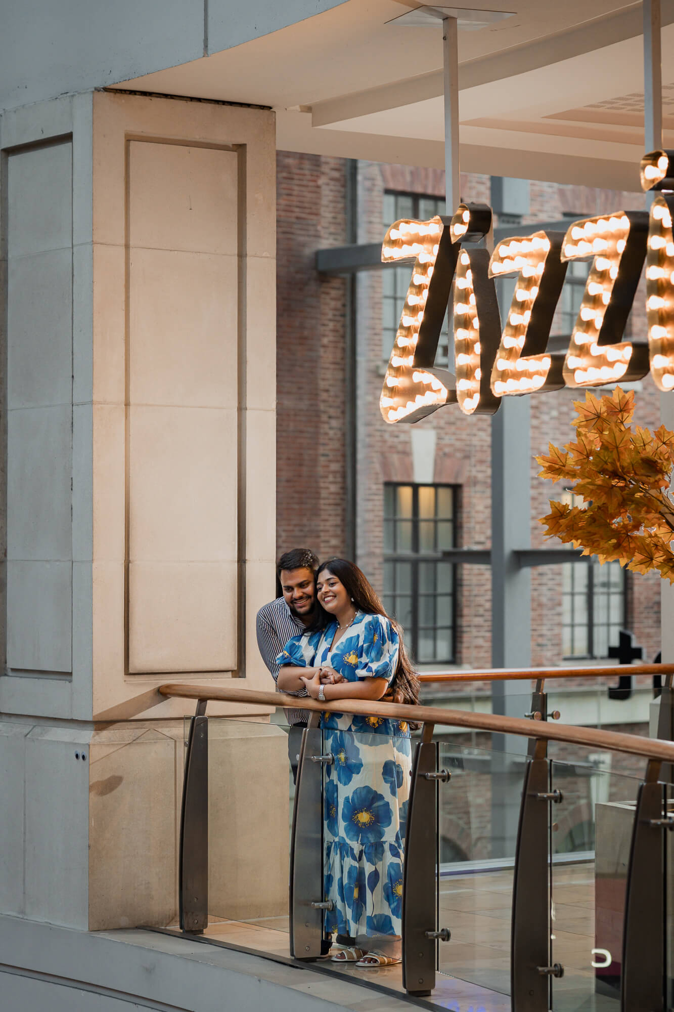 Couple embracing beneath the illuminated Zizzi sign in Leeds city centre.
