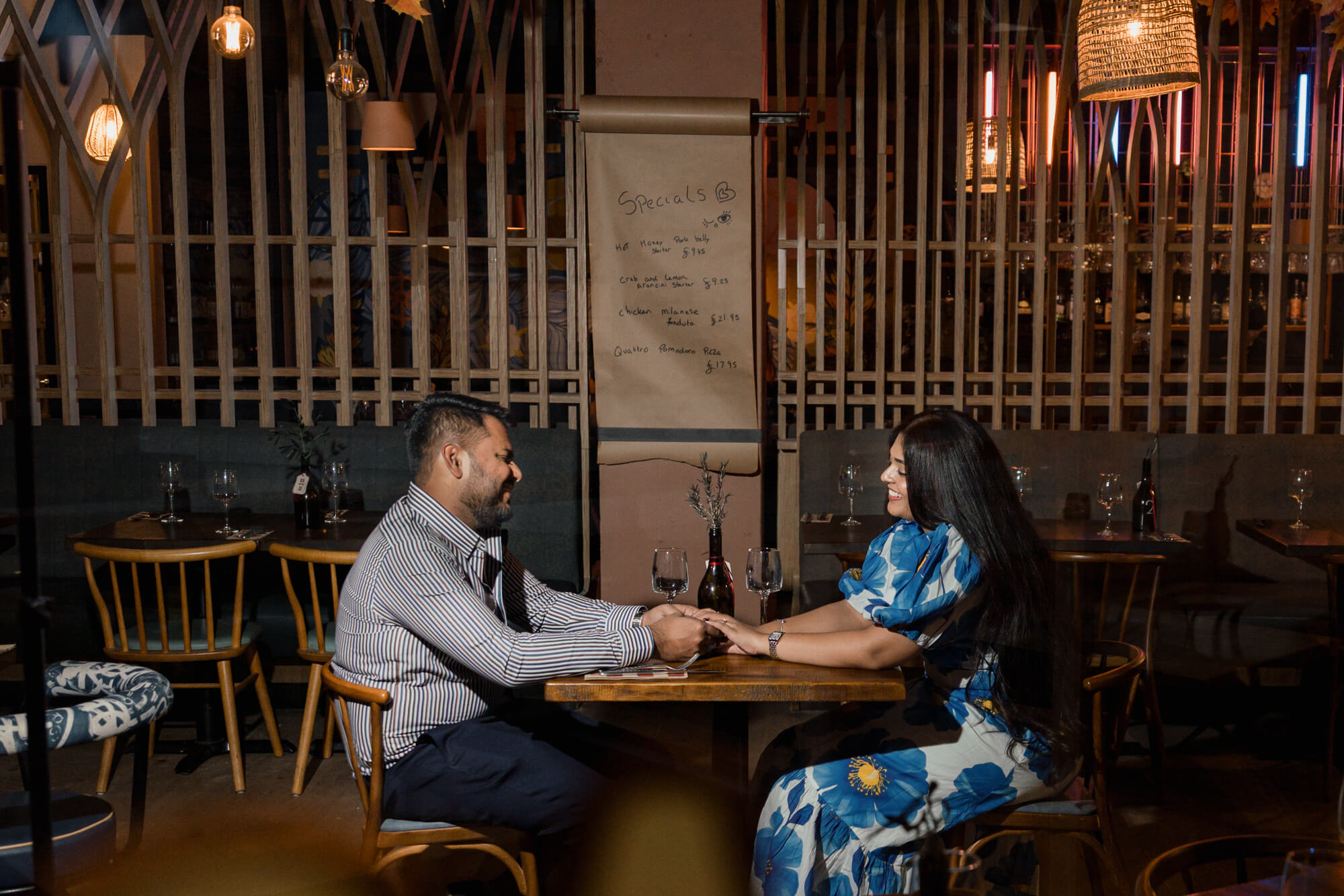 Romantic couple holding hands across a restaurant table during a Leeds engagement photoshoot.