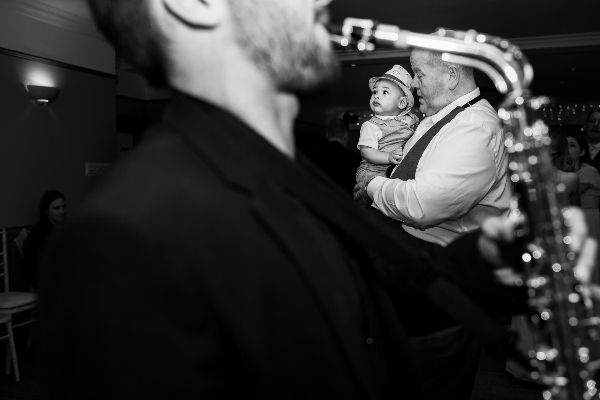Candid black and white wedding reception photograph of a child watching a musician