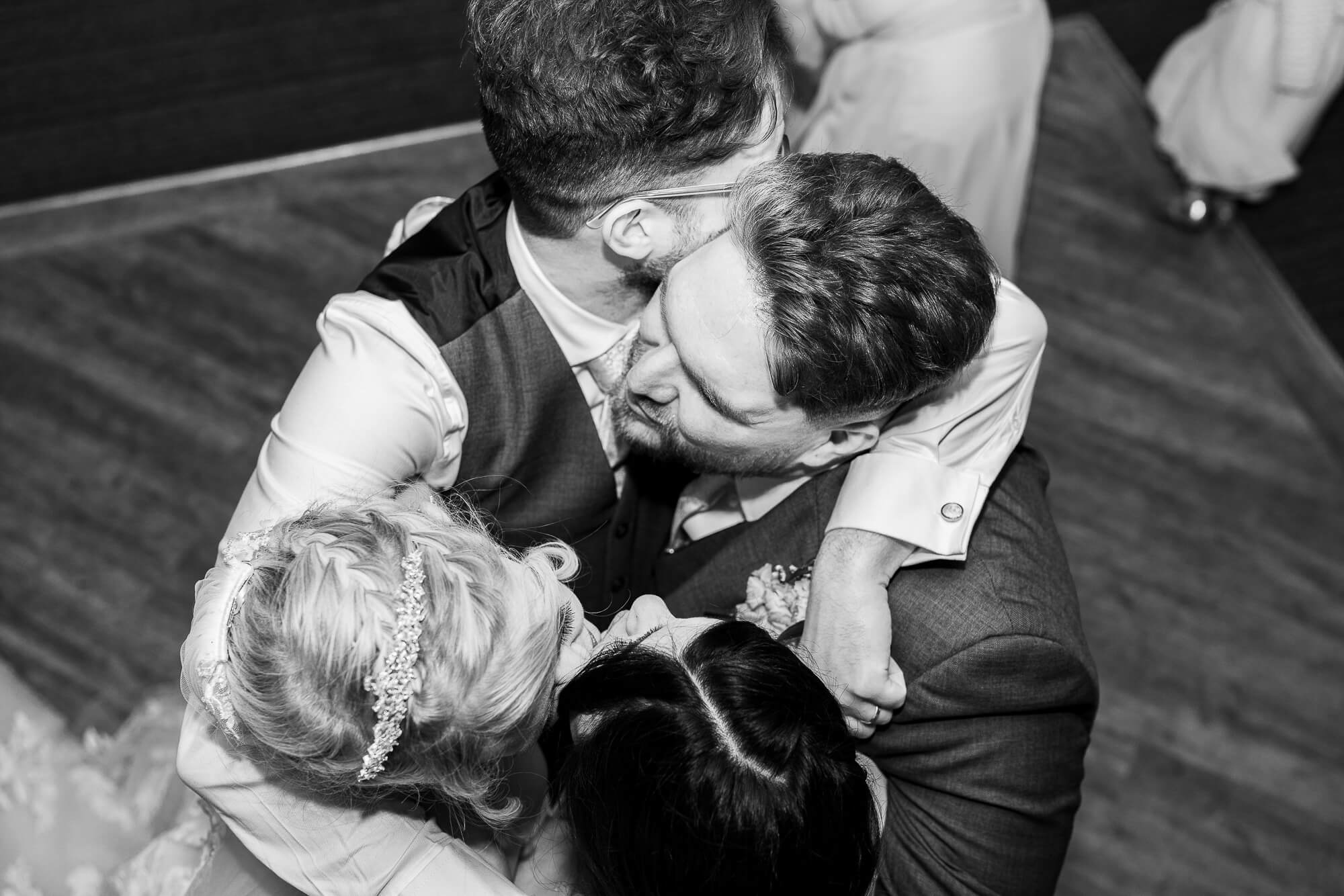 Candid black and white wedding photograph of friends embracing