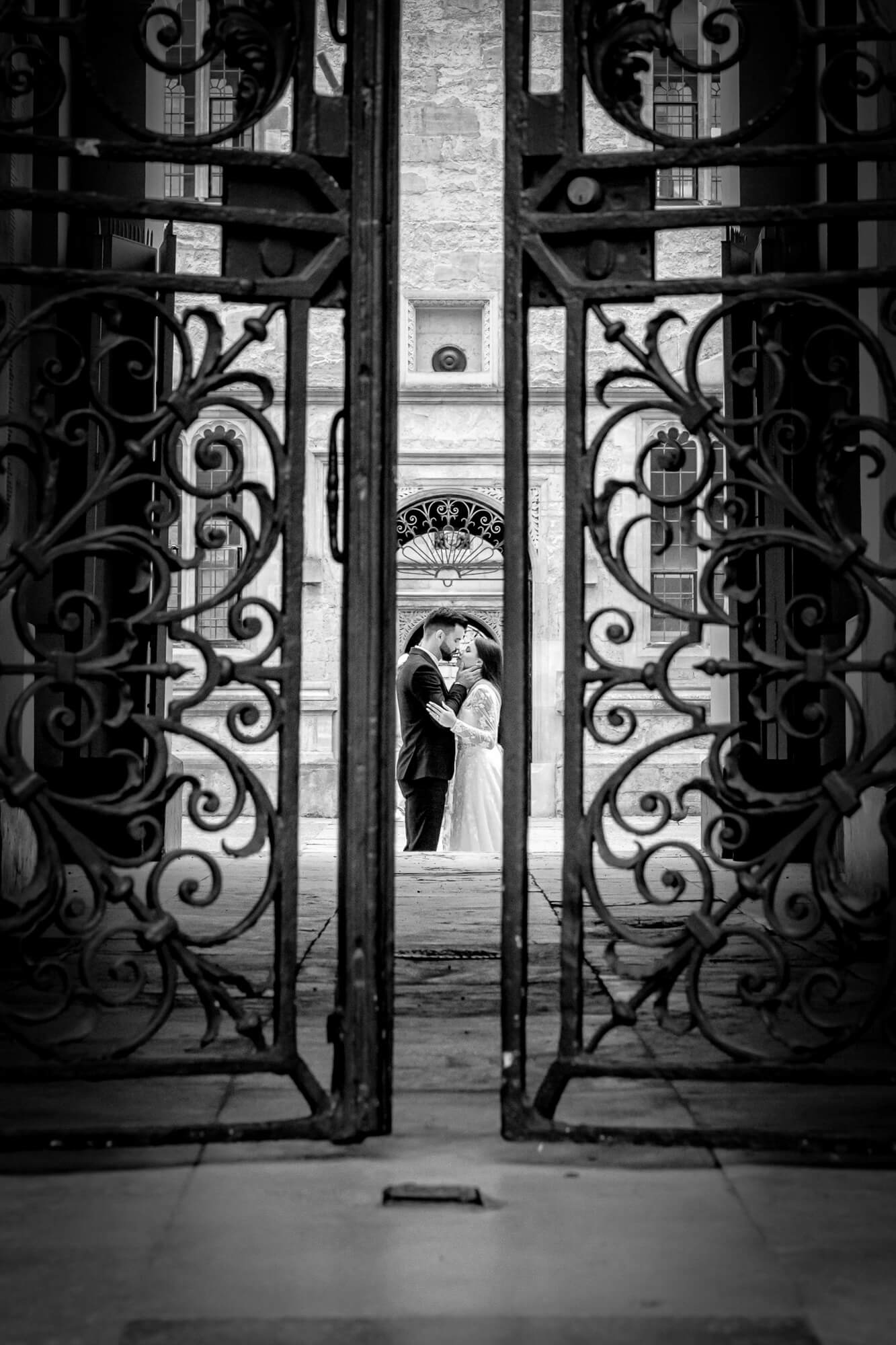 Timeless black and white wedding photograph of a couple framed by ornate gates