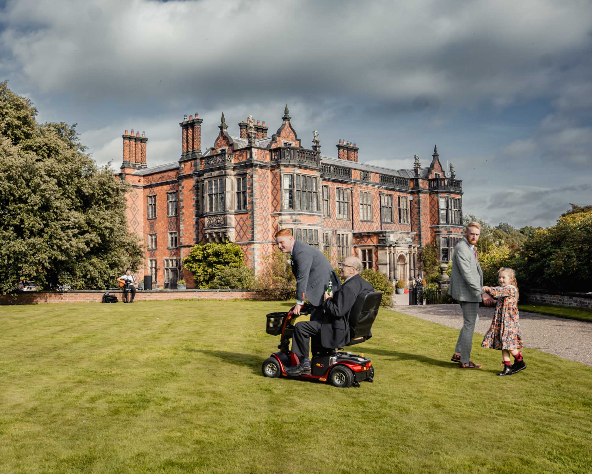 Grandad having fun with grandchild on a wheelchair accessible vehicle in front of Arley Hall during the wedding.