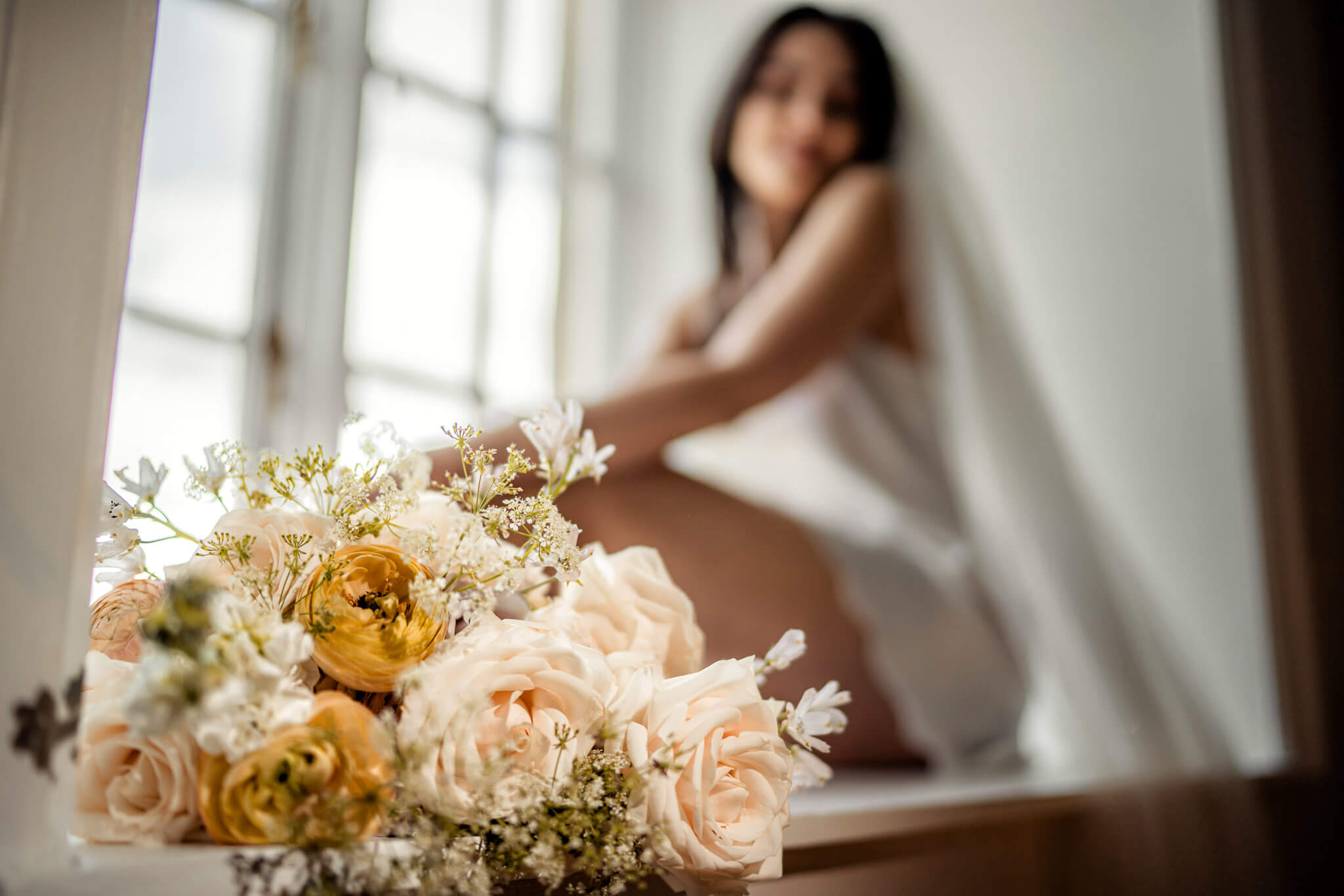 Bride sitting in the window at Hazlewood Castle, holding her legs into her arms and admiring her wedding bouquet.