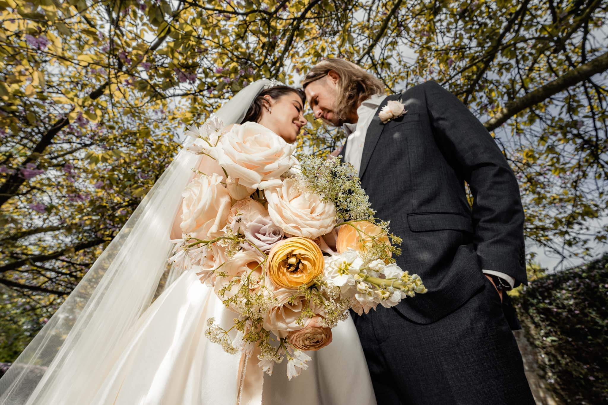 Groom and bride at Hazlewood Castle touching foreheads and holding the wedding bouquet in front of them.