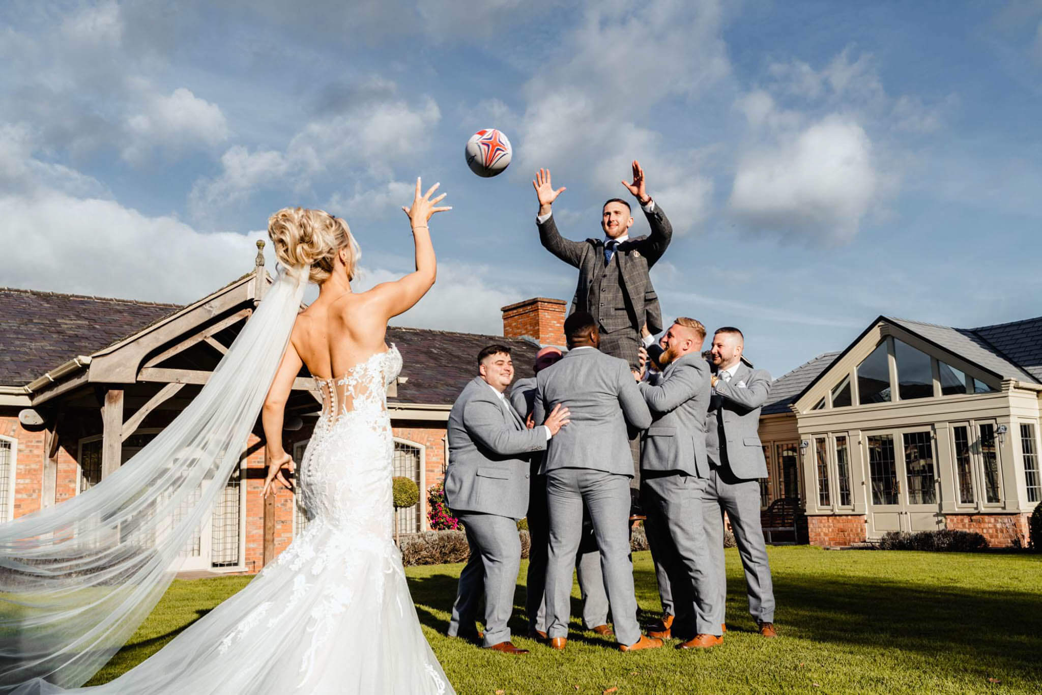 The Bride is throwing the rugby ball to the groom while the groom is lifted by his grooms men. 