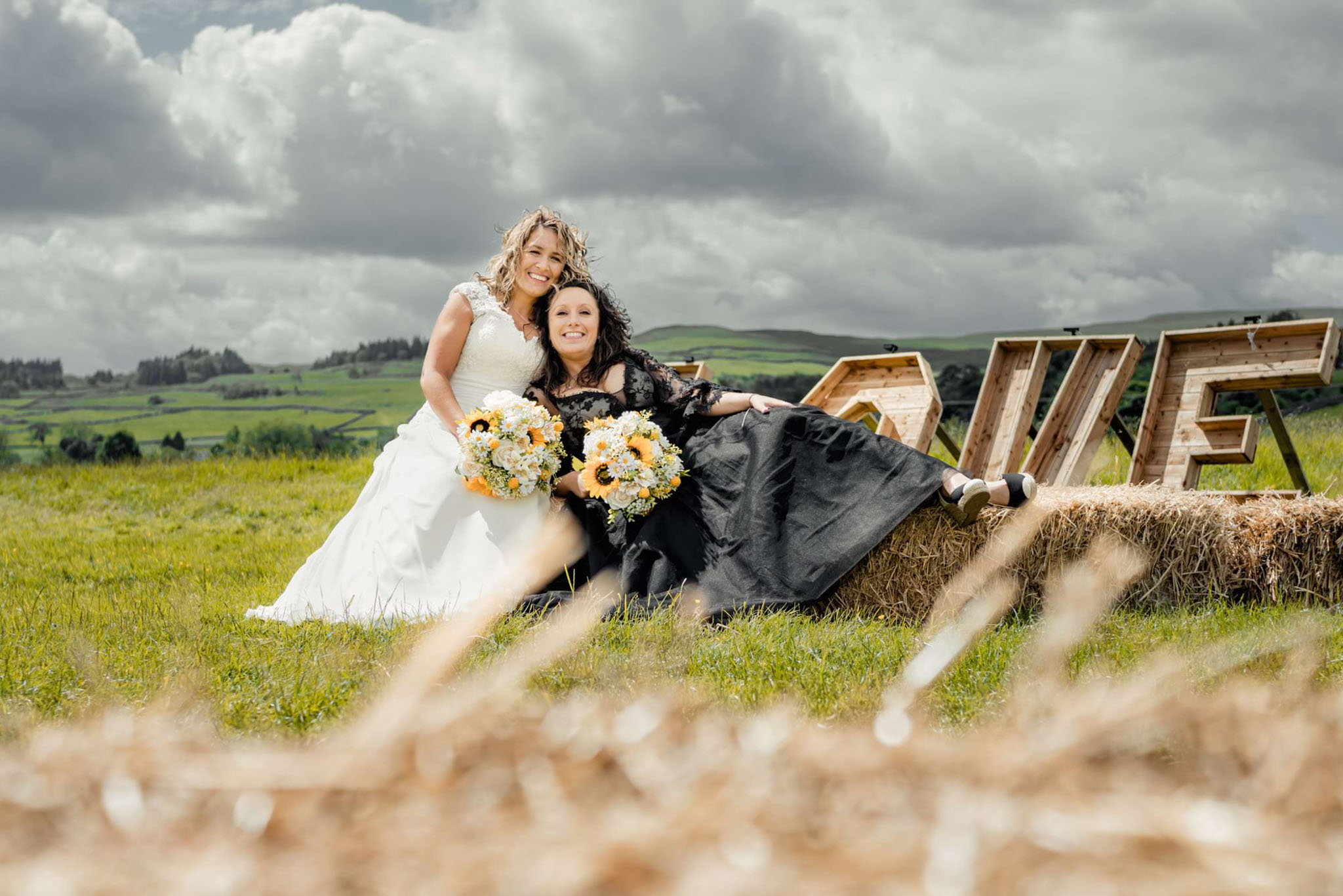 If you want to gain a average salary as a wedding photographer in the UK you need to know how to use the natural light into your favour. This picture is illustrating two wonderful brides sitting on the straw bales. One wearing a white wedding dress and the other a black one